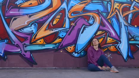 A-woman-sitting-in-front-of-a-colorful-graffiti-wall,-contemplating
