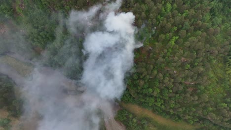 Devastating-forest-fire-just-started-in-green-hillside-after-long-dry-period-and-warm-climate---Birdseye-aerial-looking-down-at-smoke-from-steep-mountain-with-river-below