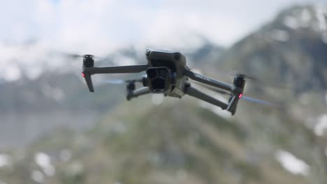 DJI-Mavic-3-Pro-Hovering-And-Swaying-In-Air-With-Bokeh-Background-Of-Snow-Capped-Mountains-In-Switzerland