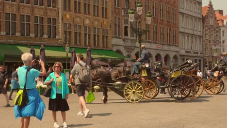 Turistas-Tomando-Fotografías-Con-Un-Carruaje-Tirado-Por-Caballos-En-La-Plaza-Central-De-Brujas,-Bélgica