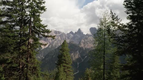 Unveil-the-majestic-mountains-of-Monte-Cristallo-near-Cortina-d'Ampezzo-as-the-drone-weaves-through-trees,-capturing-the-breathtaking-cinematic-aerial-footage-of-the-mountains