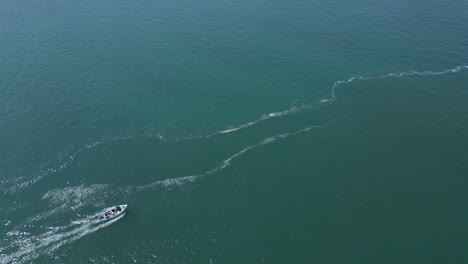 Aerial-shot-small-fishing-vessel-leaving-a-dock-on-deep-blue-Atlantic-sea-in-Portugal-near-portinho-da-arrabida