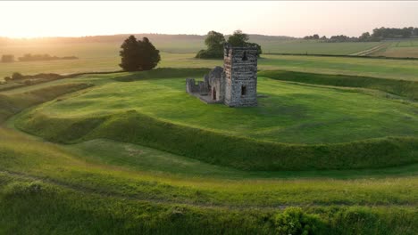 Low-level-aerial-view-of-Knowlton-Church-at-sunrise,-Dorset,-England