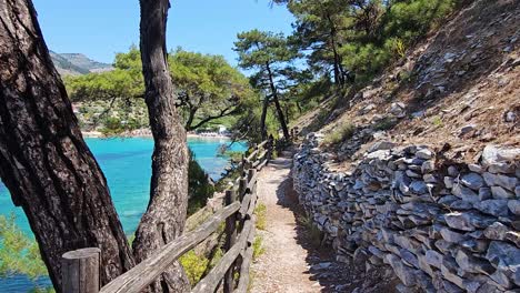 Hiking-Near-Aliki-Beach,-With-Tall-Trees-And-Lush-Vegetation-On-the-right-Side-And-The-Mediterranean-Sea-Shoreline-On-The-left,-Thassos,-Greece