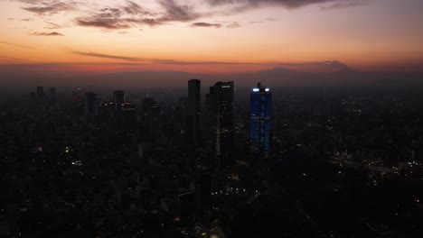 Beleuchtete-Wolkenkratzer-In-Der-Innenstadt-Von-Mexiko-Stadt,-In-Der-Abenddämmerung---Panorama-Drohnenaufnahme