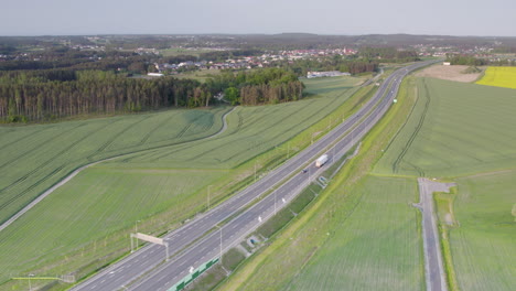Large-white-semi-truck-drives-along-highway-through-countryside-entering-city