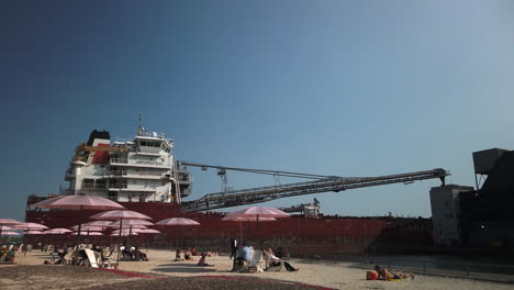 Totale-Aufnahme-Von-Sonnenanbetern-Am-Sugar-Beach,-Im-Hintergrund-Ein-Großes-Schiff,-Das-Fracht-Entlädt