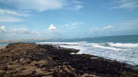 Tilt-up-shot-of-small-waves-crashing-into-algae-covered-rocks-in-the-popular-tropical-Tibau-do-Sul-beach-where-the-atlantic-ocean-meets-the-Guaraíras-Laggon-in-Rio-Grande-do-Norte,-Brazil