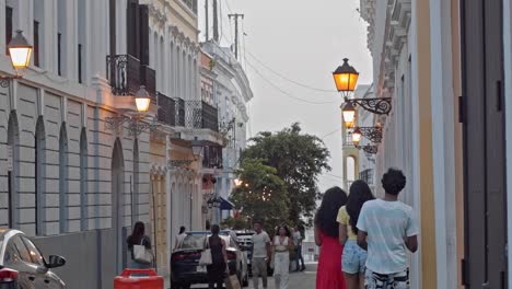 Street-view-of-colonial-style-buildings-in-Viejo-San-Juan,-Puerto-Rico-as-people,-cars-and-tourists-walk-by