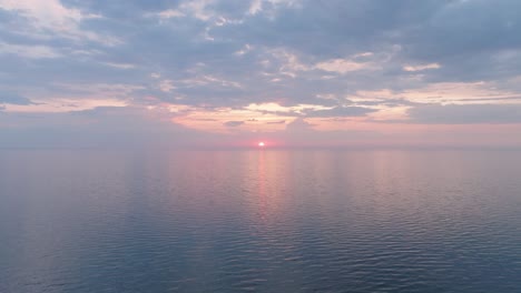 Beautiful-aerial-view-of-vibrant-high-contrast-sunset-over-calm-Baltic-sea,-clouds-at-the-horizon,-Karosta-war-port-concrete-coast-fortification-ruins-at-Liepaja,-wide-drone-shot-moving-backward