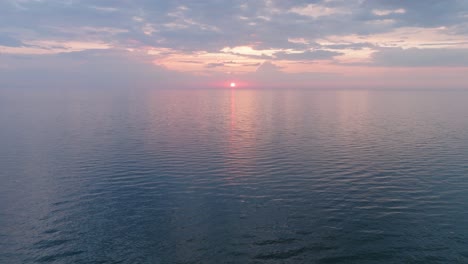 Beautiful-aerial-view-of-vibrant-high-contrast-sunset-over-calm-Baltic-sea,-clouds-at-the-horizon,-Karosta-war-port-concrete-coast-fortification-ruins-at-Liepaja,-wide-drone-shot-moving-forward