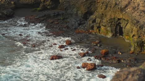 Waves-rolling-on-rocky-beach-beside-cliff-in-soft-light,-Los-Gigantes