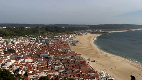 Aerial-wide-shot-of-Nazare-City-with-sandy-beach-and-Atlantic-Ocean-during-sunny-day-in-Portugal