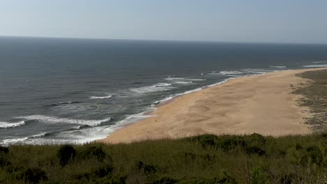 Aerial-panoramic-shot-of-empty-sandy-beach-in-Nazare-with-gigantic-waves-of-Atlantic-in-summer---slow-motion-wide-shot