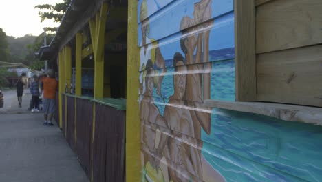 Handheld-footage-of-garifuna-men-gathering-around-an-artistically-wall-art-decor-at-street-wooden-shack-beach-bar-at-Punta-Gorda