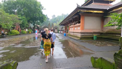 Lokaler-Balinesischer-Reiseleiter-Mit-Einem-Europäischen-Touristenpaar,-Das-An-Einem-Regnerischen-Tag-Einen-Sarong-Am-Eingang-Des-Tirta-Empul-Tempels-Trägt