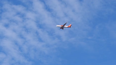 Tracking-shot-of-Easyjet-Airplane-flying-at-blue-sky-during-sunny-day,-slow-motion