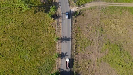 Drone-aerial-point-of-view-tracking-an-suv-car-driving-on-a-countryside-road-with-large-green-rural-areas-and-farming-landscapes,-Costa-Rica