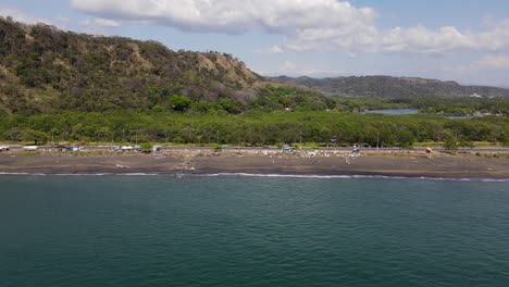 Zoom-out-aerial-drone-view-of-Port-Caldera,-revealing-highway-traffic-and-nature-areas-next-to-the-coast,-Puntarenas,-Costa-Rica