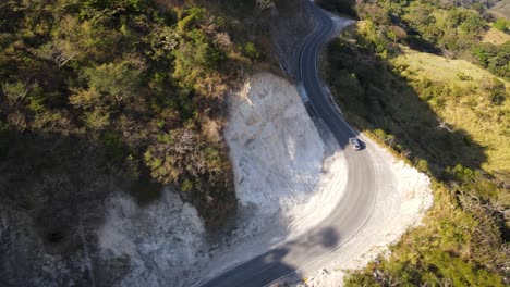 Aerial-shot-of-an-suv-car-driving-in-a-rural-road-next-to-a-hill,-in-the-nature-countryside-of-Costa-Rica,-Monteverde-natural-landscape
