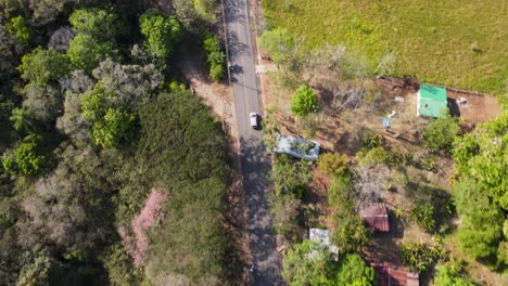 Aerial-shot-of-an-suv-car-driving-in-a-rural-road-across-farms,-trees-and-green-landscapes,-Costa-Rica