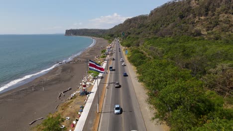 Drone-view-flying-backwards-over-the-coast's-highway-traffic-in-Port-Caldera,-Puntarenas,-Costa-Rica