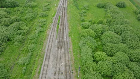Aerial-birdseye-view-of-empty-railroad-train-tracks,-countryside-scenery,-fresh-green-forest-on-the-side,-overcast-cloudy-summer-day,-wide-drone-shot-moving-forward