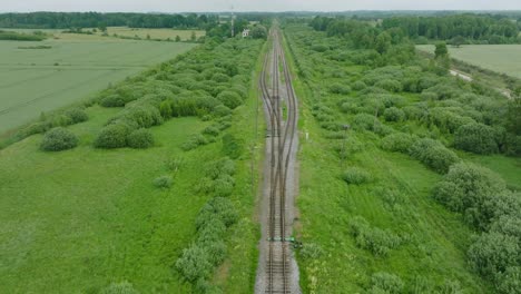 Aerial-establishing-view-of-empty-railroad-train-tracks,-countryside-scenery,-fresh-green-forest-on-the-side,-overcast-cloudy-summer-day,-wide-drone-shot-moving-forward