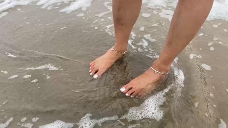 Wellen-Schlagen-Auf-Die-Beine-Eines-Mädchens-Mit-Fußkettchen,-Das-Am-Strand-Steht