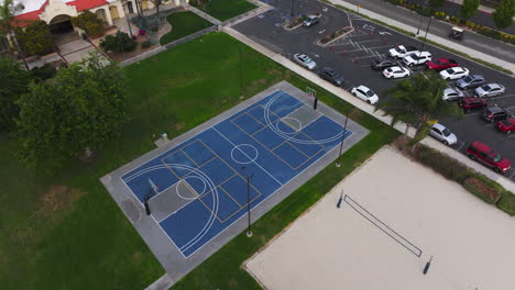 Stunning-4k-aerial-shot-of-a-vibrant-blue-basketball-court-surrounded-by-green-grass-and-beach-volleyball