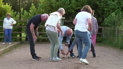 Pétanque-Spieler-Zweier-Mannschaften-Nehmen-Ihre-Kugeln-Auf,-Nachdem-Sie-Sie-In-Richtung-Eines-Cochon-Geworfen-Haben,-Um-So-Nah-Wie-Möglich-An-Ihn-Heranzukommen