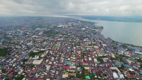 Aerial-Drone-View-Of-Urban-City-Neighborhoods,-Buildings,-And-Streets-Next-To-Ocean-Coast-In-The-Philippines