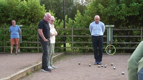 Drei-Männliche-Pétanque-Spieler-Sehen,-Wer-Bei-Einem-Ligaspiel-Dem-Cochon-Mit-Seinen-Stahlkugeln-Am-Nächsten-Ist