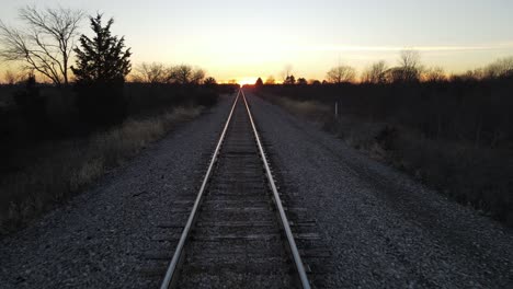 Steel-railway-tracks-shine-because-of-sunset-glow,-dolly-backward-view