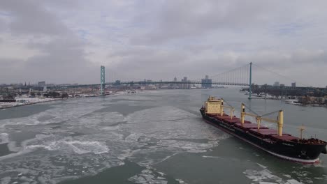 Transport-vessel-shipping-goods-on-icy-river-of-Detroit-with-Ambassador-bridge-in-background