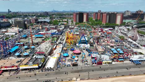 A-panning-slow-aerial-view-of-people-walking-down-the-boardwalk-at-Coney-Island-Amusement-park-with-New-York-City-in-the-background