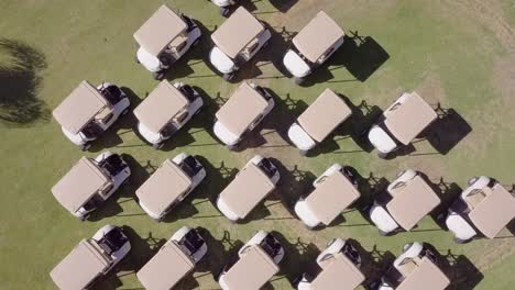 Twisting-Aerial-Shot-of-Several-Rows-of-Parked-Golf-Carts-on-Green-Grass