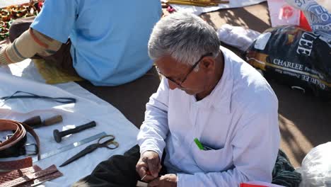 Scene-from-above-showing-an-Indian-cobbler-sewing-a-leather-belt-with-both-hands-in-his-roadside-shop
