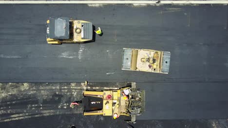 Vista-Aérea-De-Arriba-Hacia-Abajo,-Trabajadores-De-La-Construcción-De-Carreteras,-Maquinaria-Que-Coloca-Asfalto-Fresco