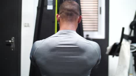 A-muscular-bodybuilder,-passionately-working-out-at-the-gym,-lifts-weights-the-camera-is-from-his-back-side
