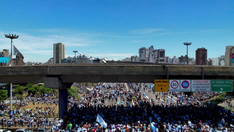 Drone-shot-over-a-bridge-in-an-Intersection-of-highways-crowded-with-jubilant-Argentinian-football-soccer-fans-marching-towards-world-cup-celebration,-waving-flags-and-cheering-for-the-winning-team