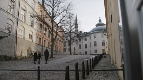 Two-adults-and-a-child-enjoy-a-Christmas-morning-walk-on-cobblestones-in-Stenbock-Palace-Riddarholmen-Gamla-Stan-Stockholm,-Sweden