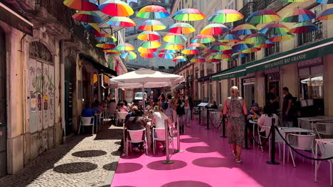 Tourist-walking-o-famous-The-Pink-Street-in-Lisbon-with-colorful-umbrella-artwork-during-sunny-day