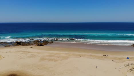 Ascending-aerial-view-of-people-on-a-calm-beach,-sunny-day-in-Australia