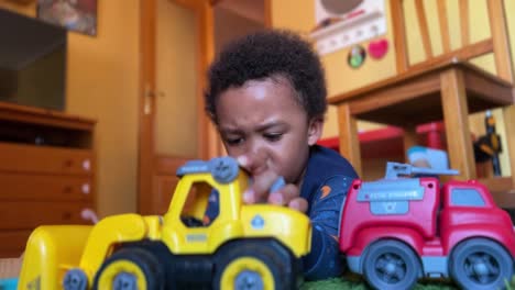 Szene-Eines-Süßen-Und-Ausdrucksstarken-3-jährigen-Schwarzen-Kindes,-Das-Zu-Hause-Spielt,-Um-Seine-Spielsachen-Zu-Reparieren,-Auf-Einem-Roten-Teppich-Liegt-Und-Einen-Blauen-Pyjama-Trägt