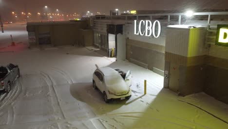aerial-footage-of-a-man-that-braves-the-heavy-snowfall-outside-an-LCBO-in-Canada,-making-his-way-to-a-waiting-white-SUV-and-entering-it