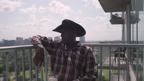 Establishing-shot-of-African-American-male-with-cowboy-hat-sitting-on-balcony