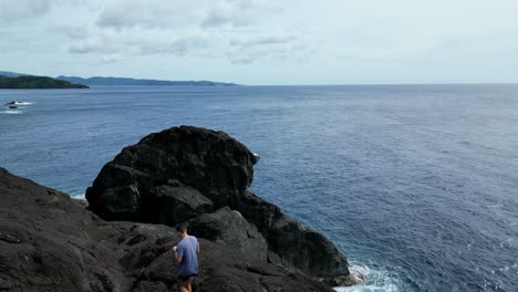 Filmische-Luftaufnahme-Eines-Männlichen-Wanderers,-Der-Durch-Basaltfelsen-Geht-Und-Die-Atemberaubende,-Weite-Meeresbucht-In-Catanduanes,-Philippinen,-Freigibt