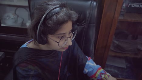 Una-Joven-Asiática-Feliz-Con-Gafas-Y-Auriculares-Trabajando-En-La-Laptop