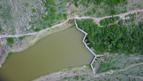 Aerial-top-down-rotating-shot-of-green-brown-dam-in-lush-mountain-valley